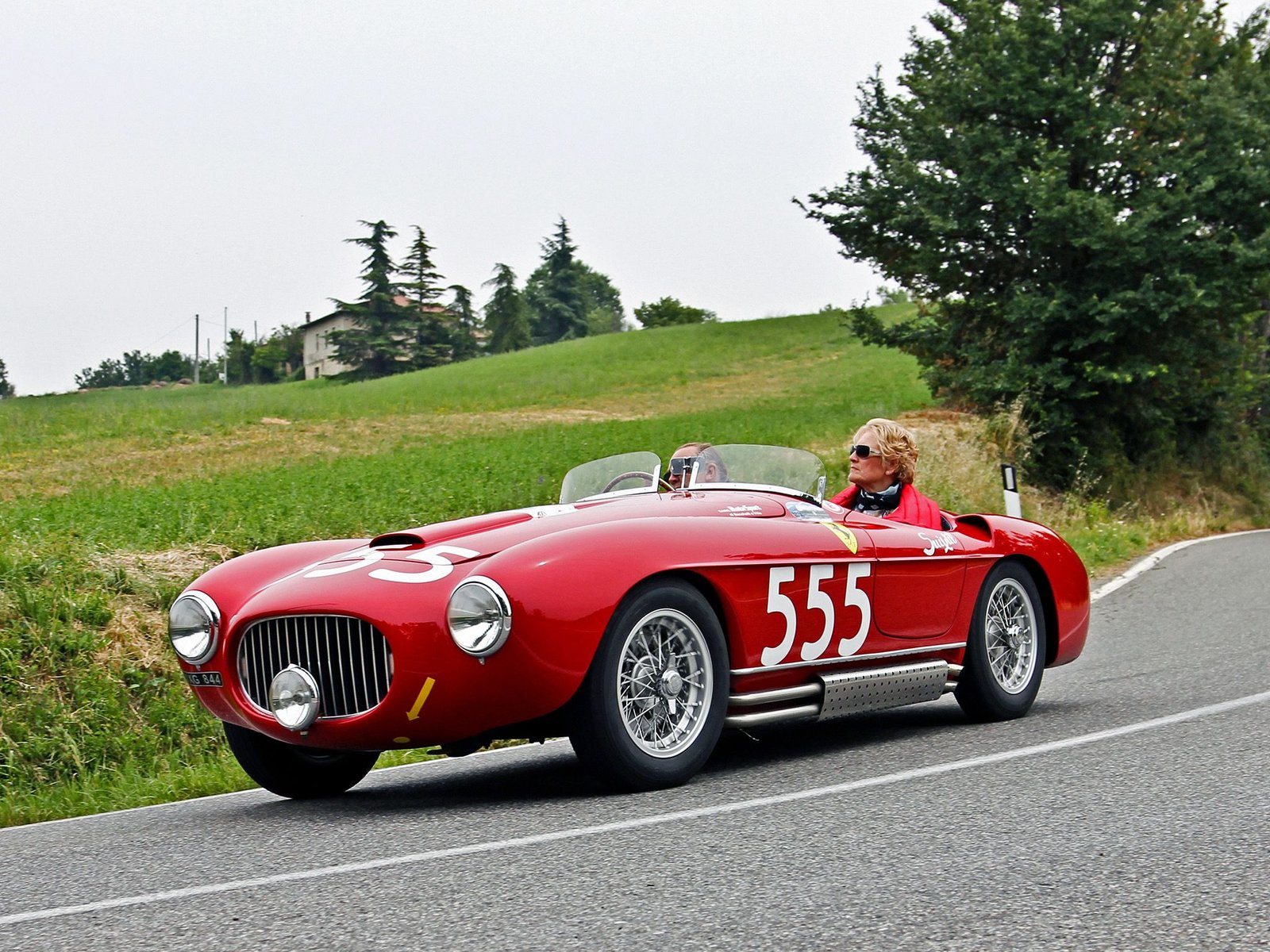 Historic red Ferrari number 555 driving on a country road